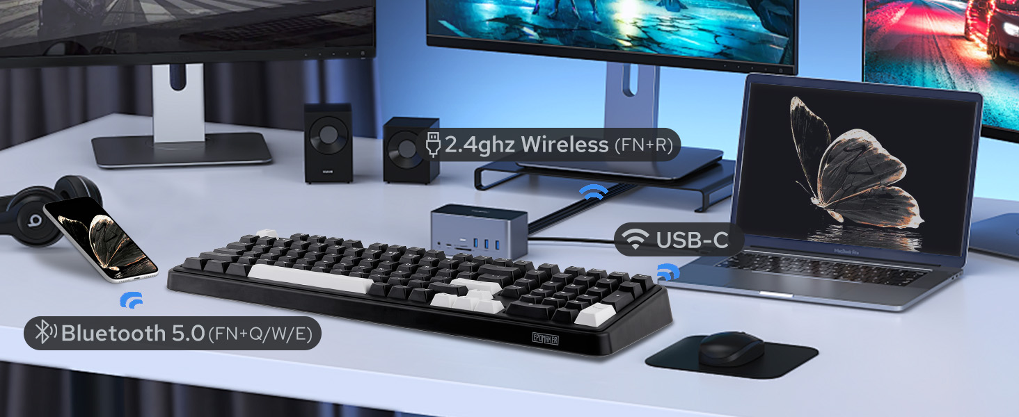 Computer desk setup with wireless keyboard, mouse, speakers, and laptop. Features USB-C connectivity, 2.4GHz wireless, and Bluetooth 5.0 capabilities. Multiple screens display nature scenes.