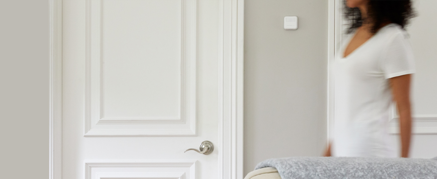 Woman walking past a Smart Room Sensor mounted on a wall in a living room