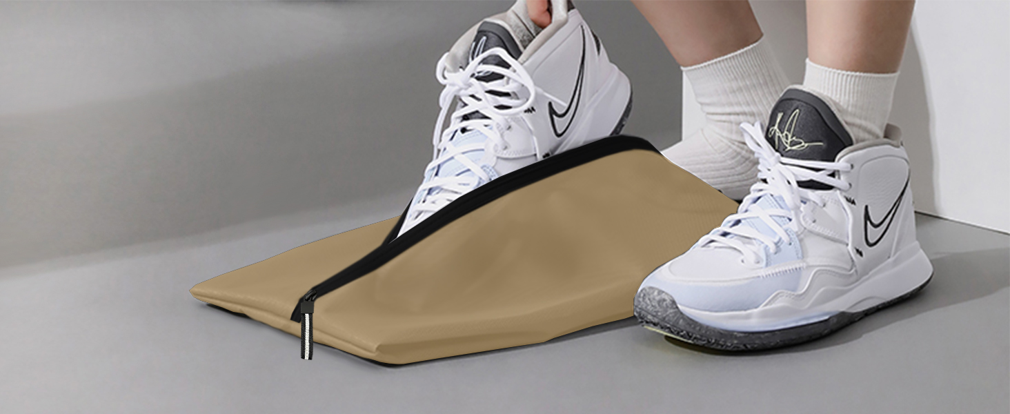 White Nike basketball shoes with black swoosh logo, worn on feet. Beside them is a folded beige fabric, possibly a bag or cover, with black zipper.
