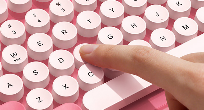 Close-up of aqua pink keyboard with round white keycaps being pressed by a finger.
