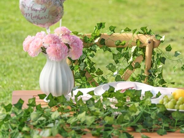Outdoor picnic setup on grass featuring pink floral arrangement, decorative items, and food display on checkered cloth with residential building background.