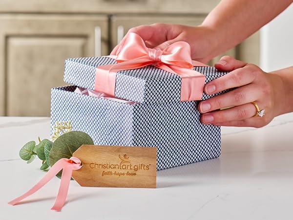 Woman packing blue gift box with pink ribbon on kitchen counter Christian Art Gifts tag