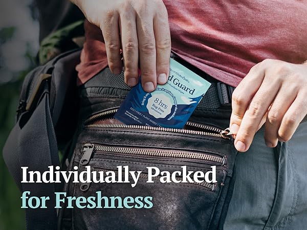 Person placing a Wild Guard Mosquito Repellent Wipe packet into a backpack pocket outdoors.