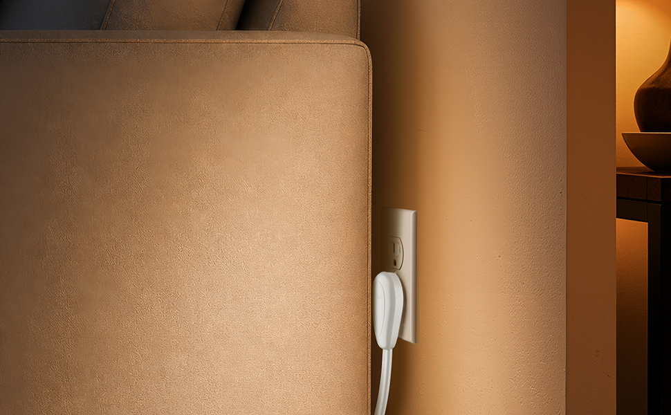 White flat extension cord plug fitting behind a leather sofa.