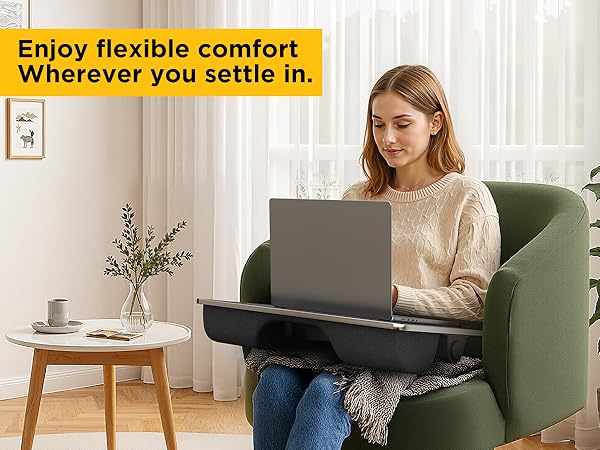 Woman using laptop lap desk with leg support while seated in armchair near bright window.