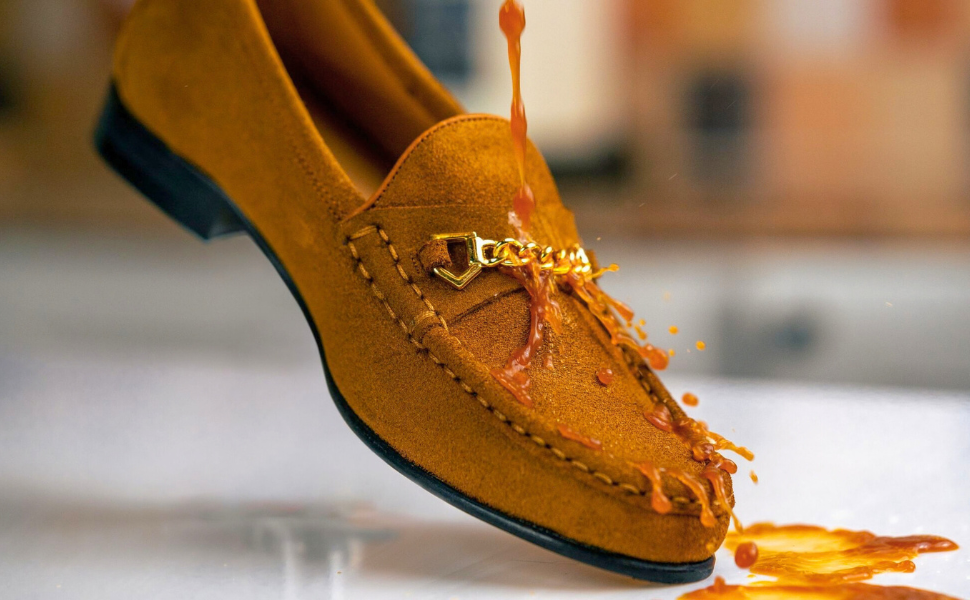 Close-up sequence of tan leather brogue shoes stepping in liquid, creating splash effect. Shows detailed wing-tip perforations and stitching pattern.