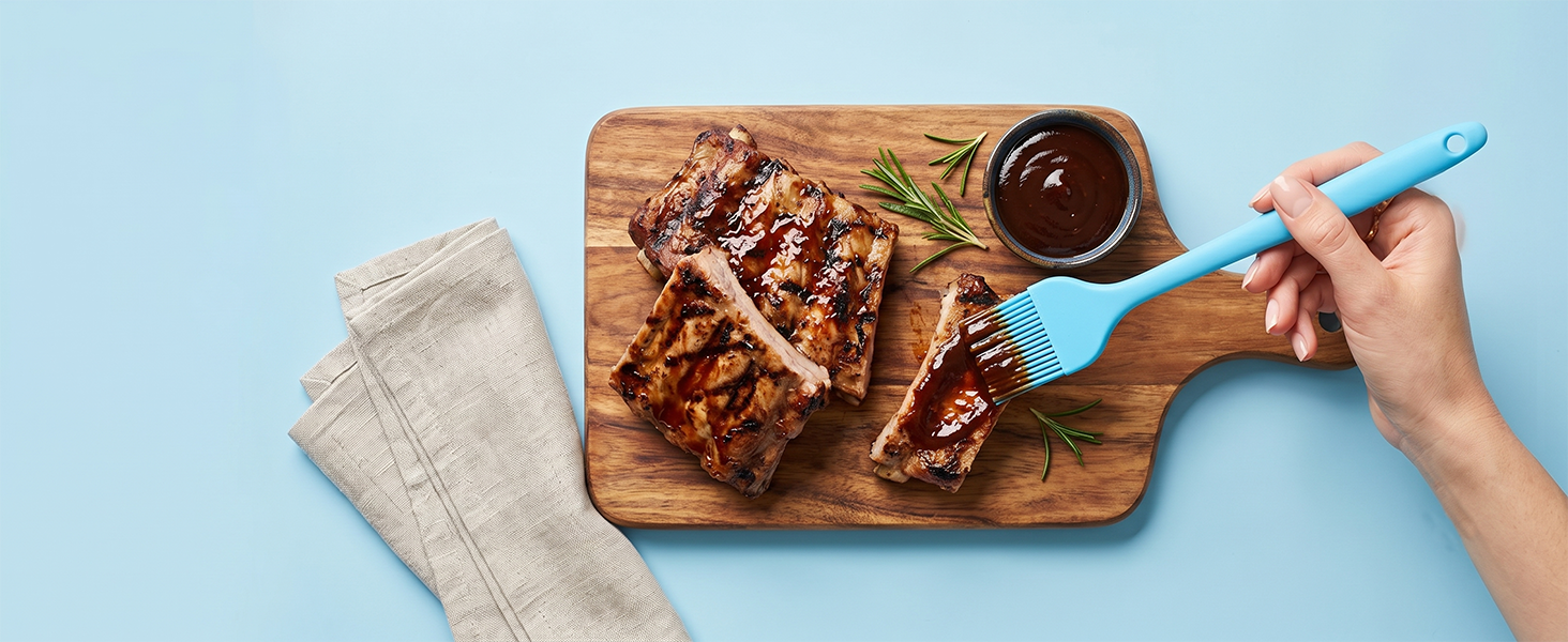 Blue silicone basting brush applying BBQ sauce on grilled ribs on pastel blue background