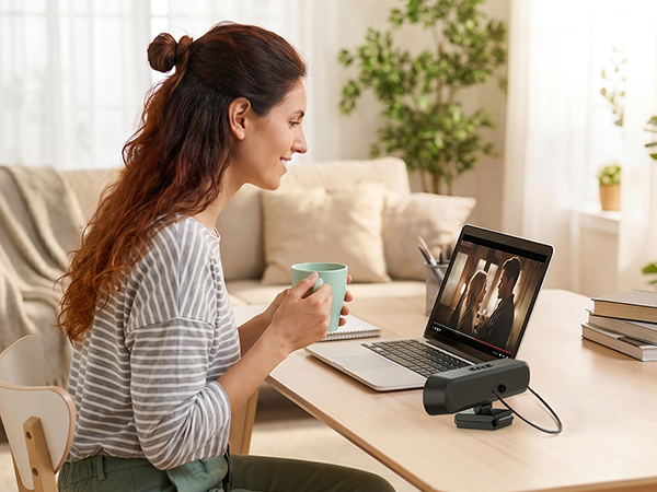 Woman with reddish-brown hair sitting at desk in striped shirt, viewing tablet device mounted on black stand with keyboard visible.