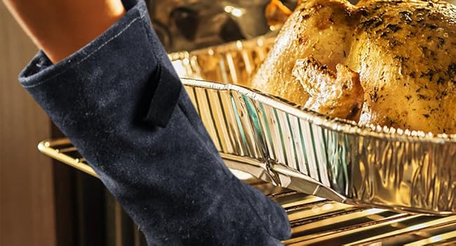 Roasted whole chicken in glass baking dish inside oven, with dark-colored oven mitt visible.