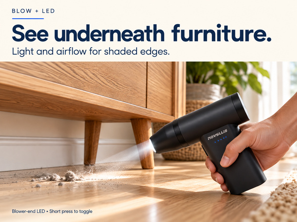 Handheld air duster with LED light illuminating loose dust beneath a wooden cabinet