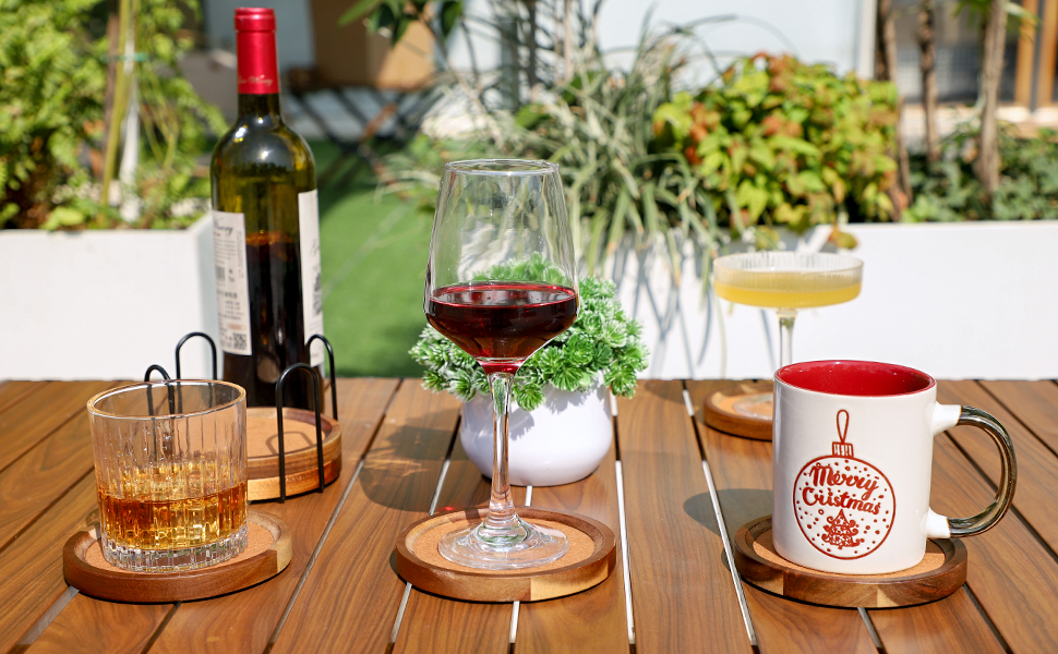 Outdoor table setting with wine bottles, glasses of red and white wine, and a red mug on wooden surface.