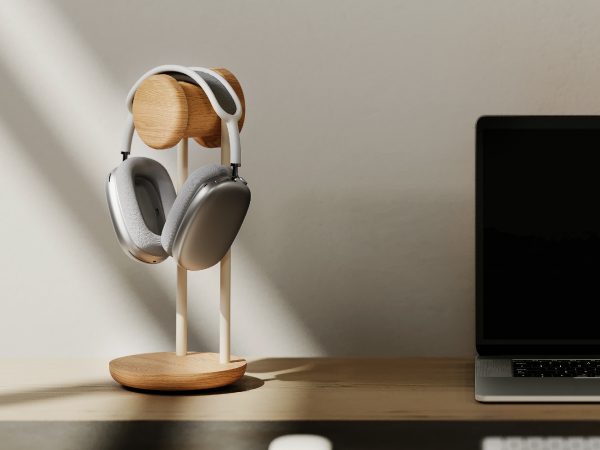 White and tan gaming headset displayed on wooden stand against neutral gray background with partial laptop visible.