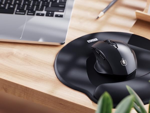 Black circular computer mouse on wooden desk, next to partial view of laptop keyboard and plant leaves.