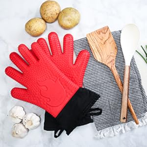 Red gloves with cooking utensils and garlic on a marble countertop.