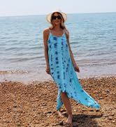 Woman wearing a long blue floral maxi dress standing on a pebble beach with ocean in the background.