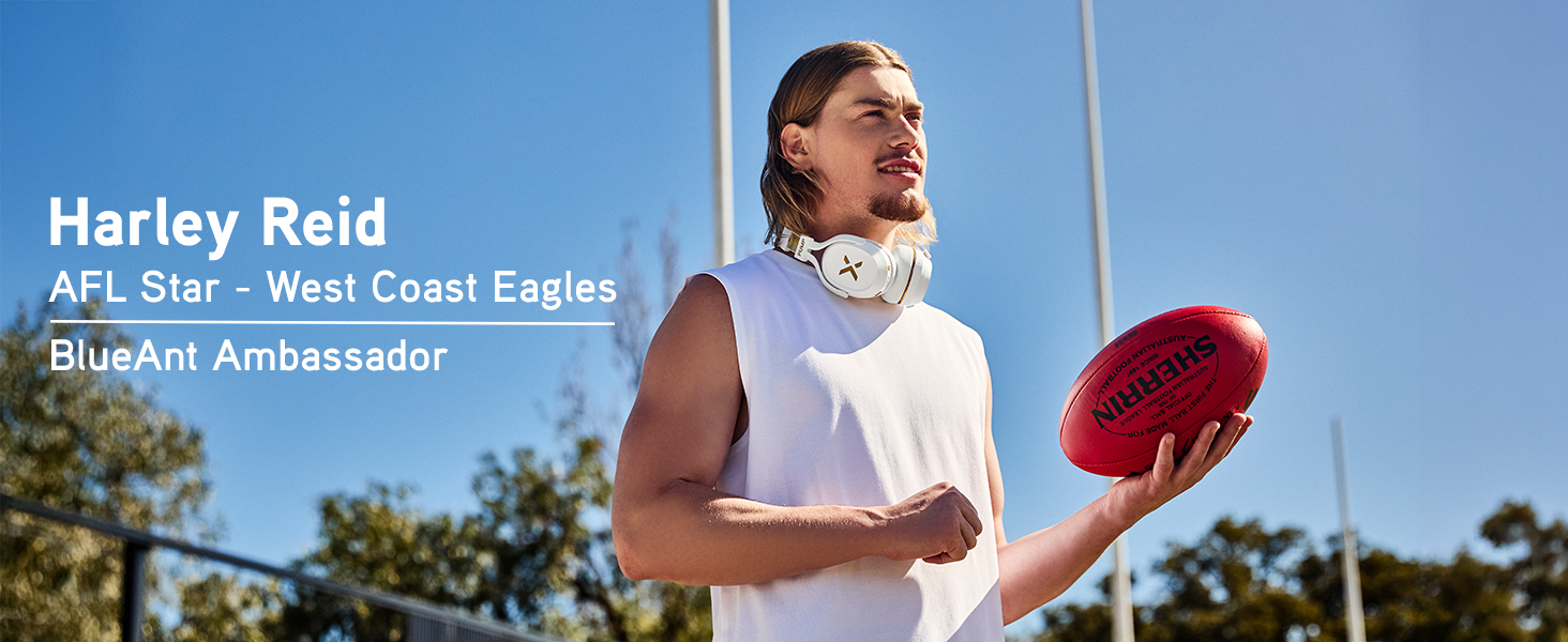 Harley Reid stands on an AFL field holding a football, wearing Pump X headphones around his neck