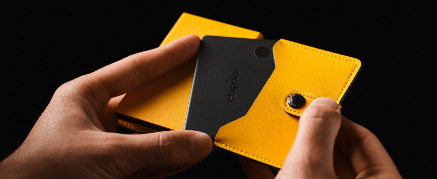 Hands holding a yellow and black bifold wallet against black background, demonstrating open compartment structure.