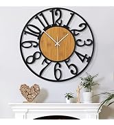 Modern wall clock with black metallic frame featuring large decorative numbers and wooden center disc, mounted above white mantle with decorative items.