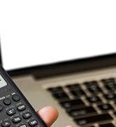 a hand holding a remote control next to a laptop.