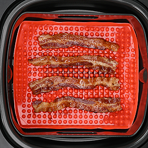 bacon cooking on raised mat inside air fryer