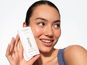 Smiling woman with fresh skin holds Native Blood Orange & Clove deodorant, looking confident.