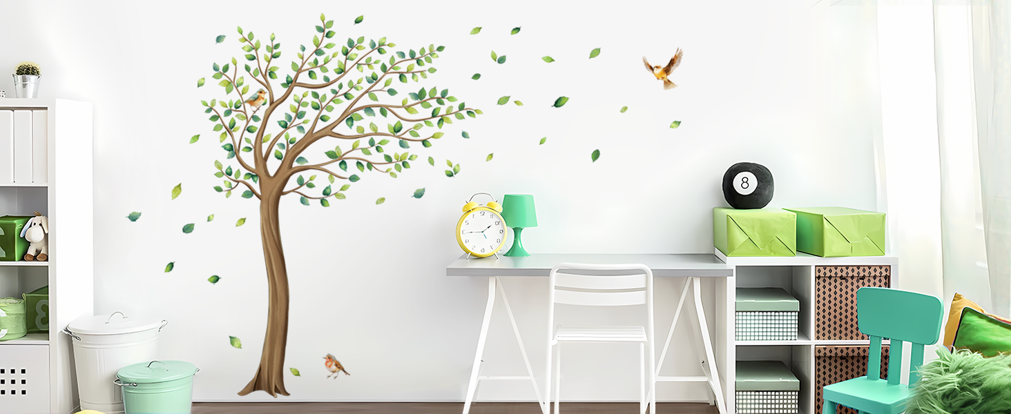 Wall decal of a green tree with falling leaves, next to a white desk with colorful chairs in a bright room with storage shelves.