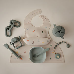 Flatlay of mushie silicone feeding tableware. Bib, placemat, more feeding essentials.