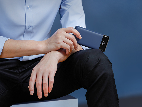 Person wearing blue shirt holding a slim, rectangular smart device on their wrist. Device has a dark screen with visible display.