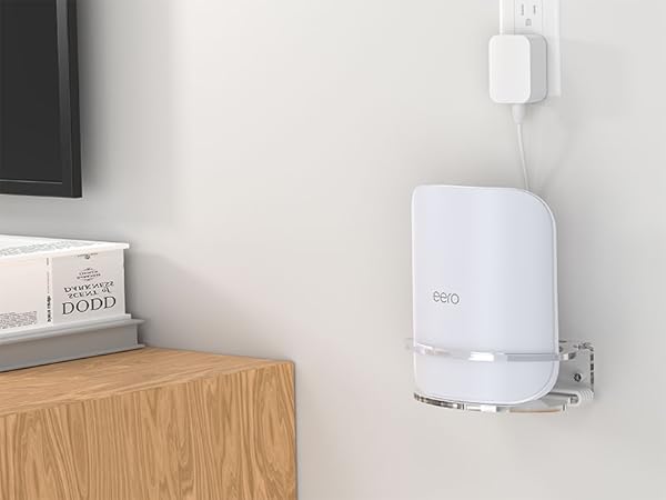 White cylindrical device mounted on wall next to wooden furniture, appears to be a smart home or electronic device with subtle LED indicator.