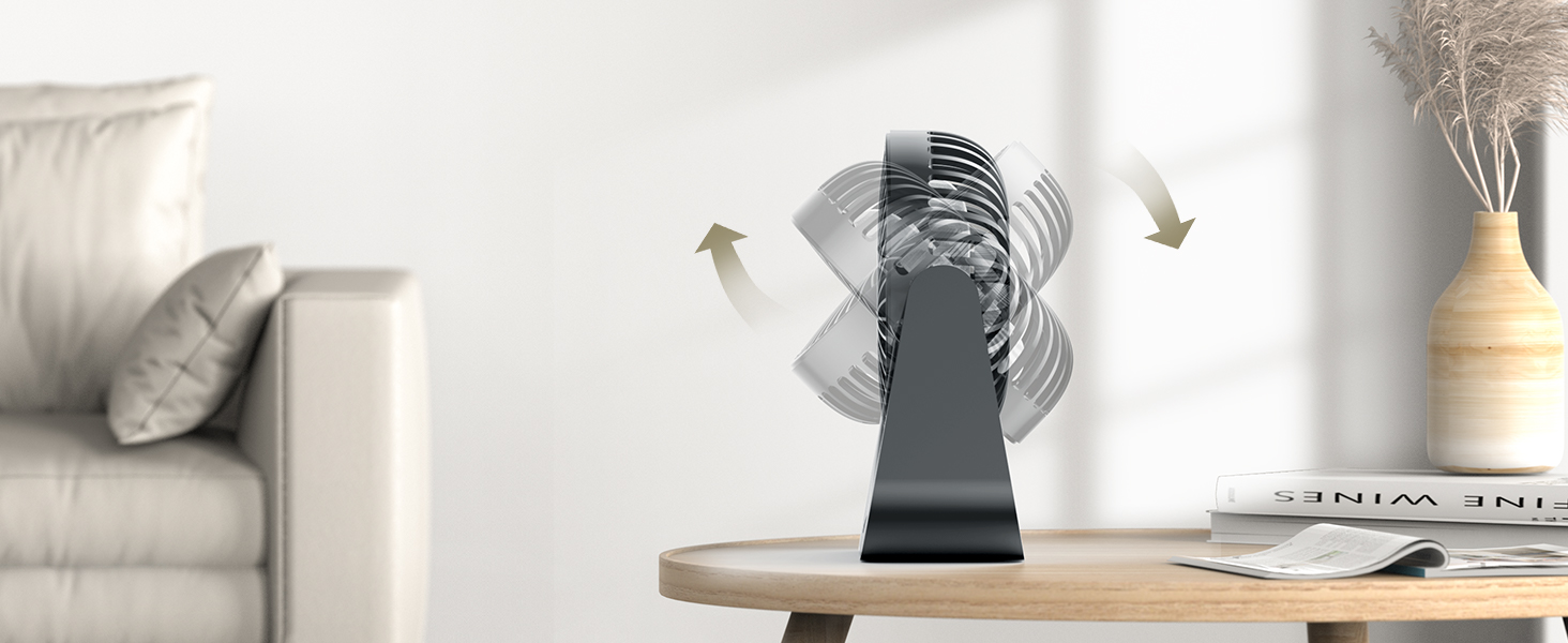 Portable desk fan on a coffee table in a living room setting, with decorative items and a couch visible in the background.