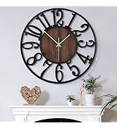 Large wall clock with black metal frame featuring oversized numerals. Central wooden disc with white clock hands. Decorative items visible below.