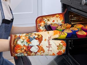 Decorative oven mitts with colorful autumn-themed pattern being used to handle something from an oven.
