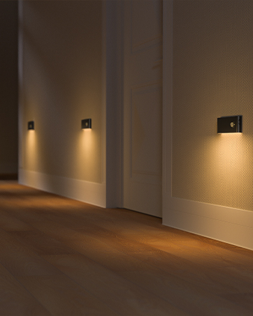 Three rectangular wall sconces mounted on white walls, emitting warm light downwards. The sconces create a cozy ambiance in a hallway with wooden flooring.