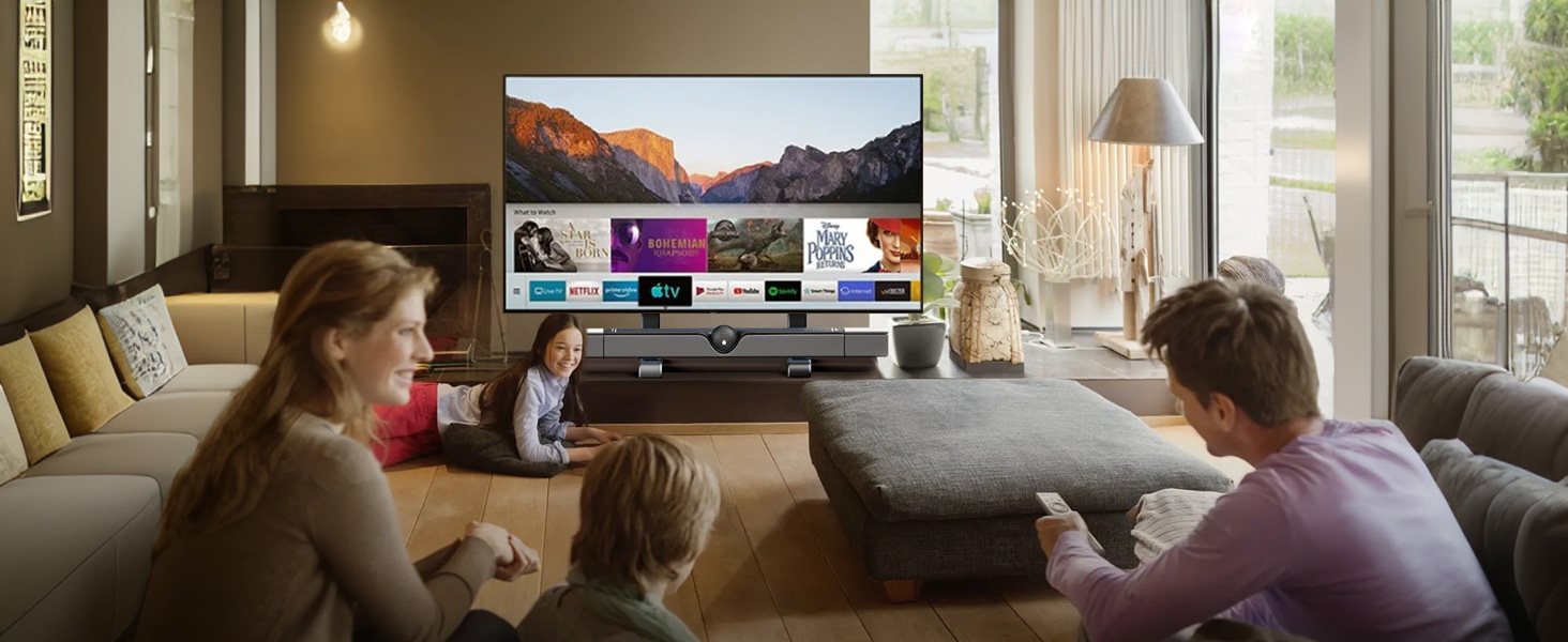 Living room scene with two people sitting on gray sofa watching television showing colorful content, natural window lighting, modern interior setting.