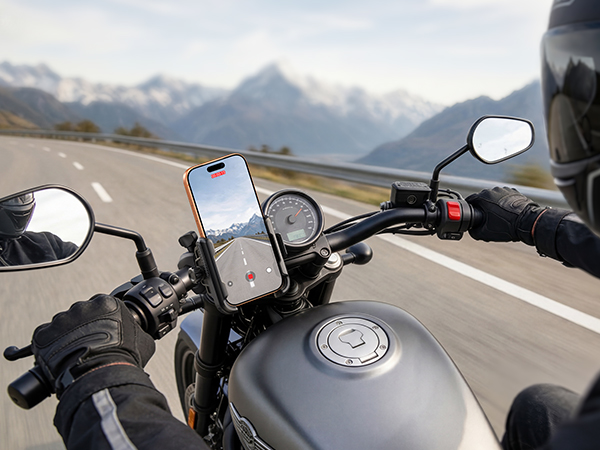 First-person view from motorcycle handlebars while riding on a curved mountain road, showing speedometer and road ahead.