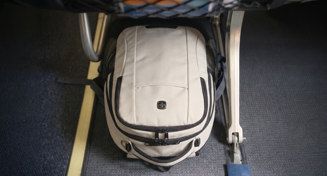 Overhead view of a cream laptop backpack fitting under an airplane seat as a personal item
