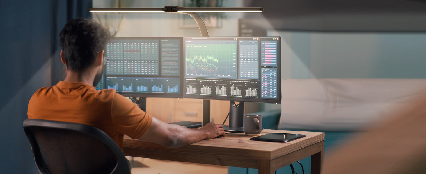 Person seated at desk working with multiple computer monitors displaying data or programming interface.