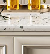 Terrazzo countertop with embedded colorful stone chips, partially visible. White cabinet with decorative molding below. Gold-toned tray with glass bottles on top.