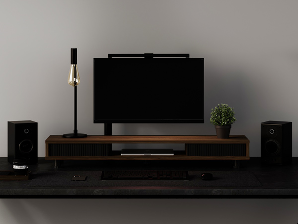 Modern living room entertainment setup with large flat-screen TV, wooden media console, floor lamp, and speakers against gray wall.
