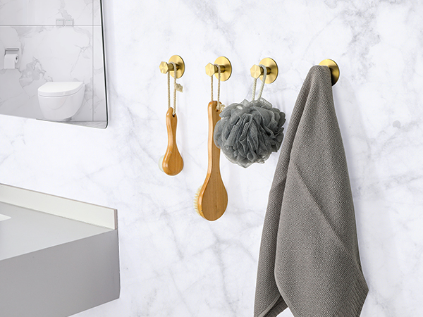 Gold bathroom hooks with wooden handles, holding a gray towel and shower puff against a marble-patterned wall. A toilet is partially visible.