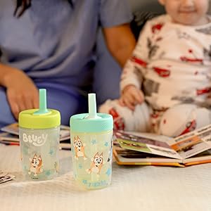 Two Bluey kids tumblers with silicone straws in foreground, with mother and son reading picture book