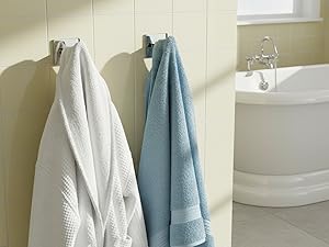 Modern bathroom interior featuring a freestanding white bathtub, beige walls, and hanging blue and white towels on wall-mounted racks.