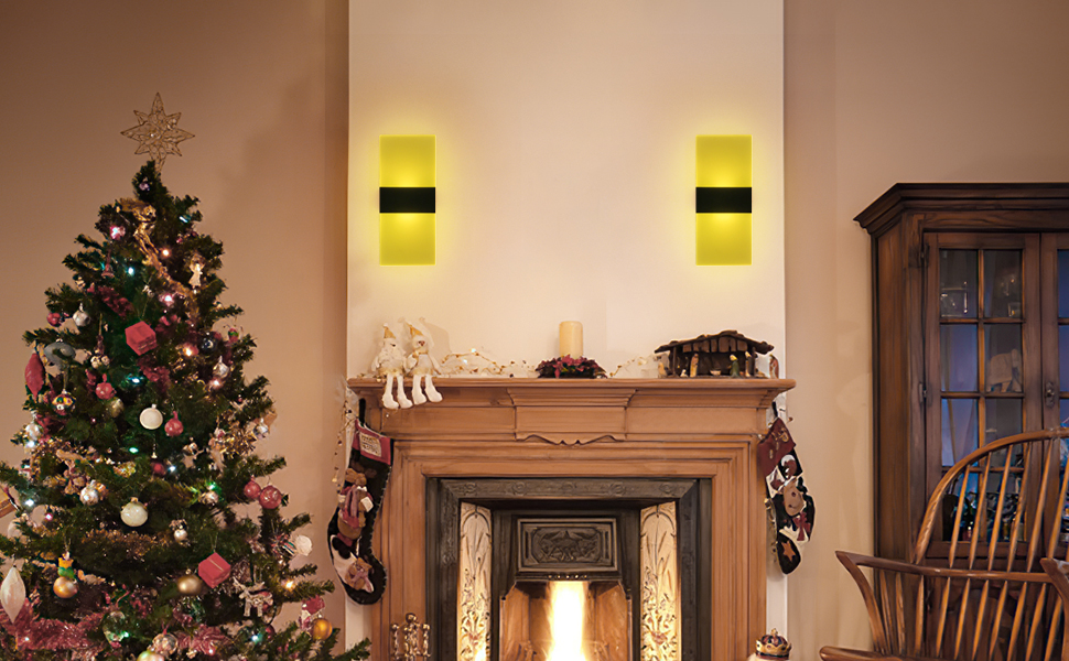 Cozy living room with decorated Christmas tree, lit fireplace, and wooden mantel. Two yellow wall sconces provide warm lighting. Stockings hang from the mantel.