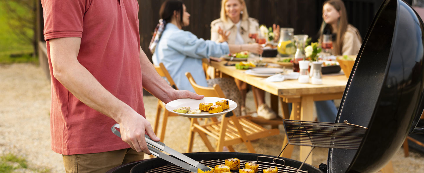 Outdoor barbecue scene with person grilling food on a charcoal grill. In the background, people are seated at a table enjoying a meal.