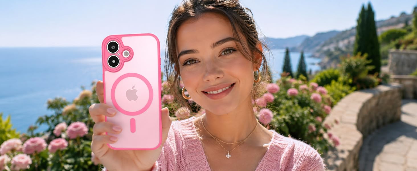 Young woman holding pink smartphone case with circular design element, smiling at camera with scenic Mediterranean coastal landscape and flowers visible in background.