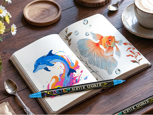 Open sketchbook or notebook displaying colorful illustrations of marine life including blue dolphins and orange fish on white pages against a wooden surface.