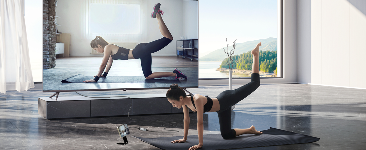 Two people performing floor exercises on yoga mats in a bright, modern space with large windows and mirror.