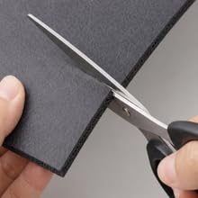 Black PU leather coffee mat being cut with scissors for a customizable fit.