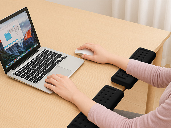 Person using laptop with wrist support pads positioned on desk surface for ergonomic comfort while typing.