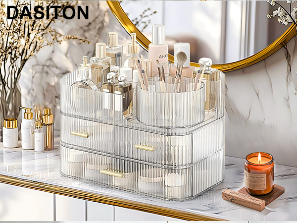 Clear acrylic cosmetic organizer with multiple compartments and drawers, displaying various makeup products and brushes. Ribbed texture on exterior, gold-tone drawer pulls visible.